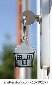 House Key On A House Shaped Silver Keyring In The Lock Of A Door