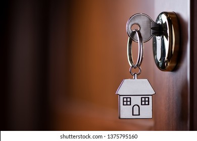 House Key On A House Shaped Silver Keyring In The Lock Of A Entrance Brown Door