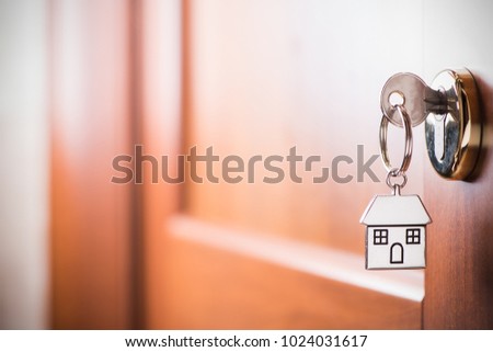 House key on a house shaped silver keyring in the lock of a entrance  brown door