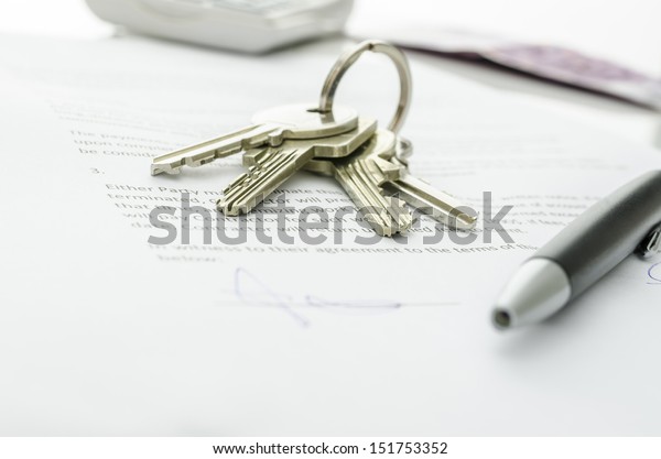 House keys and money on a signed contract of house\
sale.  Focus on keys.