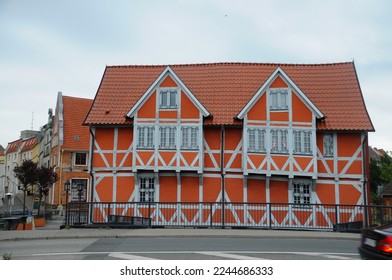 A house looks attractive for its orange and white color, brick and wooden material, and exposed wooden beam structure to embellish the entire facade.