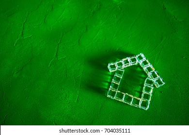 House made of ice cubes on a green background, the concept of real estate and ecology