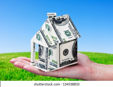 House made of money in hand on background of green field