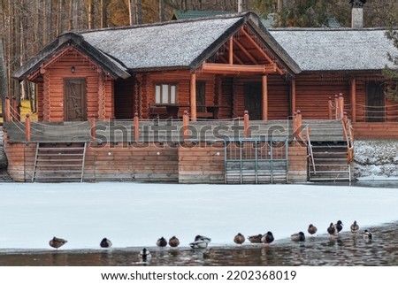 House made of wooden logs standing near the frozen lake in winter. Selective focus.