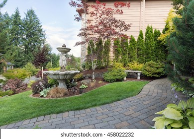 House Manicured Frontyard Garden With Water Fountain Stone Bench Green Lawn Plants Trees Shrubs And Brick Paver Walkway Path