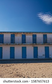 house with many blue doors on the beach against a blue sky and clouds on a bright sunny day