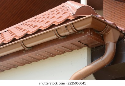 House metal rooftop with plastic rain gutter pipeline, soffit and soffit boards. Guttering house roof corner with downspout pipe in problem areas. - Shutterstock ID 2225058041
