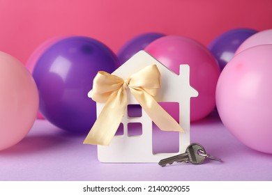 House model with bow, key and colorful balloons on violet table. Housewarming party - Powered by Shutterstock