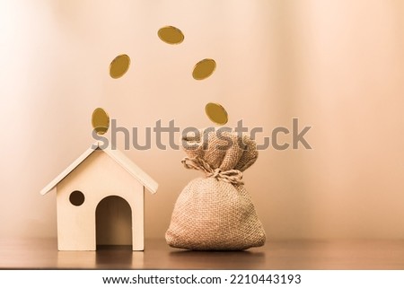 House model and coin drop to the money bag with growing interest put on the desk on brown background, Business investment or saving money to buy real estate concept.