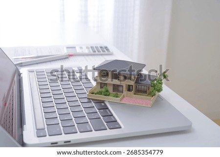A house model and a computer. The image of a real estate agent