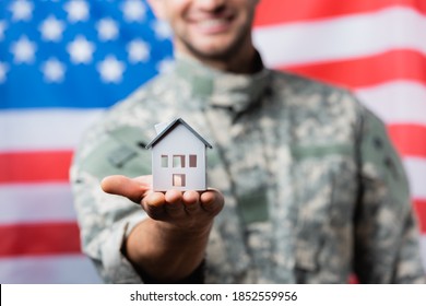 house model in hand of happy military man in uniform near american flag on blurred background - Powered by Shutterstock