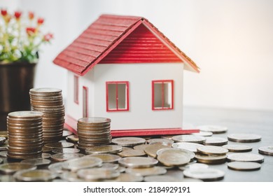 Hausmodell- und Geldmünzen stapeln sich auf unscharfem Tischhintergrund. Sparpläne für Immobilien, Darlehen, Investitionen, Hypotheken, Finanzen und Bankwesen über das Wohnungskonzept.