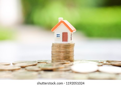 House model on gold coins stack and many coins on the floor with green background. Using for saving money, investment property and business and finance.