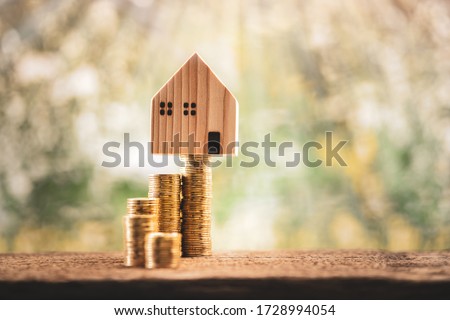 House model put on the stack gold coin with growing interest value on sunlight in the public park, Saving money or loan for business investment real estate or buy a new home for a family concept.