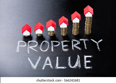 House Models On Stacked Coins Showing Property Value Concept On Blackboard