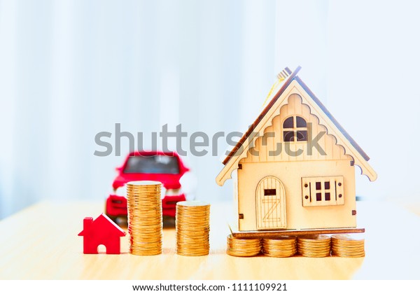 House models and red car models and gold coins placed\
on wooden boards.Credit or loan and earning for home and car in the\
family.Use money to exchange or buy in business and real estate.   \
  