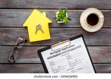 House mortgage with application, house toy, keys, glasses, coffee on wooden banker desk background top view