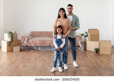 House Move, Renovation And Repair Concept. Full Body Length Of Cheerful Young Family Of Three People Standing In New Empty Apartment, Posing And Looking At Camera, Hugging, Free Copy Space