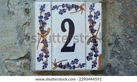 House number 2 sign. Traditional Italian home sign board painted on ceramic tile Placed on the wall. Number two. painted lavender flower pattern. Concrete wall background. 