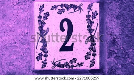 House number 2 sign. Traditional Italian home sign board painted on ceramic tile Placed on the wall. Number two. painted lavender flower pattern. Concrete wall background. 