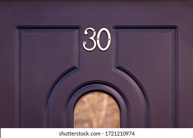 House Number 30 On A Dark Blue Wooden Front Door With Rounded Grooves And A Glass Panel