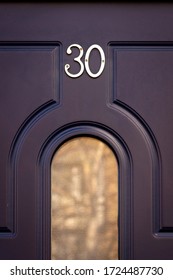 House Number 30 On A Dark Blue Wooden Front Door With Rounded Grooves And A Glass Panel