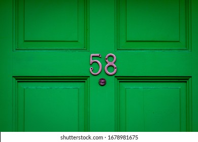 House Number 58 On A Green Wooden Front Door, Which Is Weathered And Has A Peephole