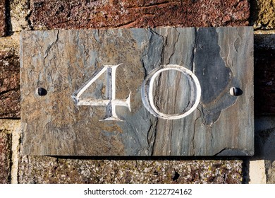House number forty painted white on a subtly textured and coloured slate base screwed to a red brick wall