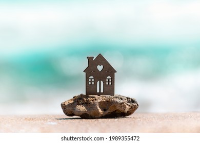 House On Sea Beach Symbol Of Dream Real Estate, Family Vacation, Seaside Resort. House On Natural Sea Stone On Blurred Sea Background. Insurance, Property, Rental Housing Concept