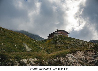 House on top of the mountain. Lonely house in the fog. Cottage on a green hill. Wooden building on a cliff. Alpine hotel. Grassy cliffs. Tourist place. Beautiful valley. Mountains background