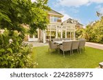 a house with an outdoor dining area in the back garden and patio, surrounded by lush green plants on a sunny summer day