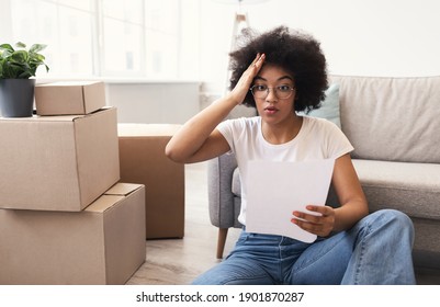 House Ownership And Rent Problem. Shocked African Woman Reading Paper Bill Or Sale Agreement Sitting Among Moving Boxes Indoors. Mortgage And Renting Deal, Real Estate Issues Concept