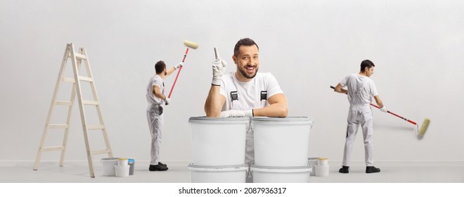 House painter leaning on buckets and pointing up and other painters painting a wall isolated on white background