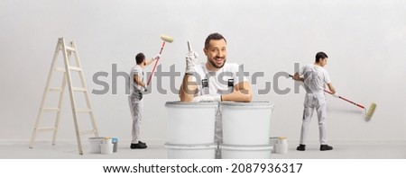 House painter leaning on buckets and pointing up and other painters painting a wall isolated on white background