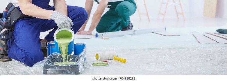 House painter pouring green wall paint into tray - Shutterstock ID 704928292