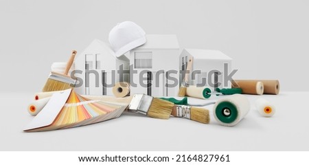 house painter tools, brushes, paint rollers, paper masking tape and colors swatches on desk with model house, supply and service in color shop in the hardware and store of building material.