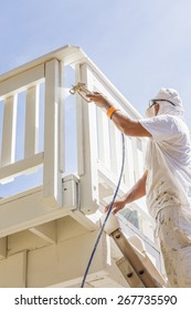 House Painter Wearing Facial Protection Spray Painting A Deck Of A Home.