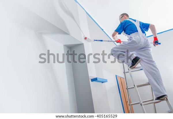 House Painting and Renovation\
Business Concept. Caucasian Male Painting House Room From the\
Ladder.