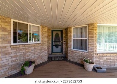 House porch with bricks and potted plants at the front door with oval panel behind the screen door. There is a bay window on the right and sliding window on the left with reflective glass panes.