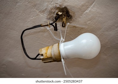 House problems, unsafe work concept. Photo of a lighting installation with an old ceramic light bulb socket improvised electrical wire connection