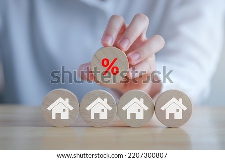 House and property investment and asset management concept. Interest rates, loan mortgage, house tax, sale discount. Hand holding red percentage sign icon from  wooden blocks with house icon.