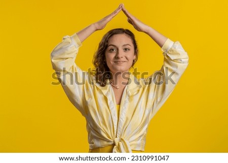 House roof about head. Young woman playing childish catching up game, feeling in safe making roof above head with hands, insurance, security service. Girl isolated alone on yellow studio background