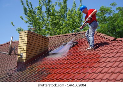 House roof cleaning with pressure tool. Worker on top of building washing tile with professional equipment. Moss removing with water.