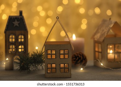 House Shaped Holders With Burning Candles On Grey Table Against Blurred Christmas Lights