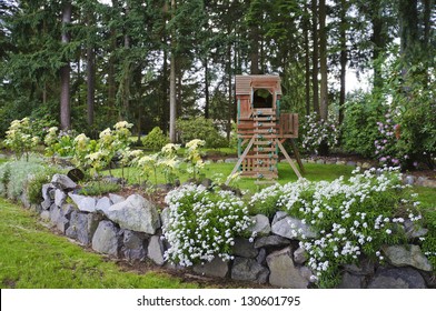 House Spring Backyard With Rock Wall And Kids Playground With Wooden Swing And Slide.