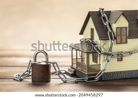 House tied with a chain and a closed lock. The concept of a ban on the sale of real estate, house arrest.