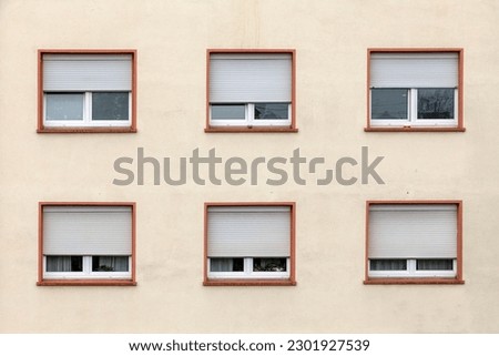 house wall with windows with partly closed plastic shutter in harmonic row