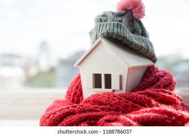 House In Winter - Heating System Concept And Cold Snowy Weather With Model Of A House Wearing A Knitted Cap