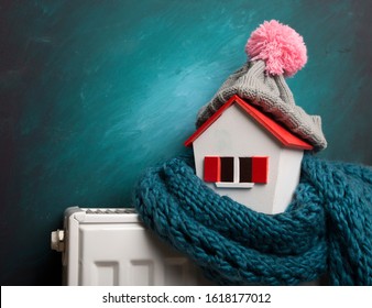 House In Winter - Heating System Concept And Cold Snowy Weather With Model Of A House Wearing A Knitted Cap