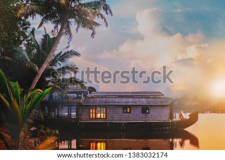 A houseboat is anchored in a lake at the Kerala Backwaters in India. The shot is taken during sunrise with the sun and beautiful cloudy sky in the background.